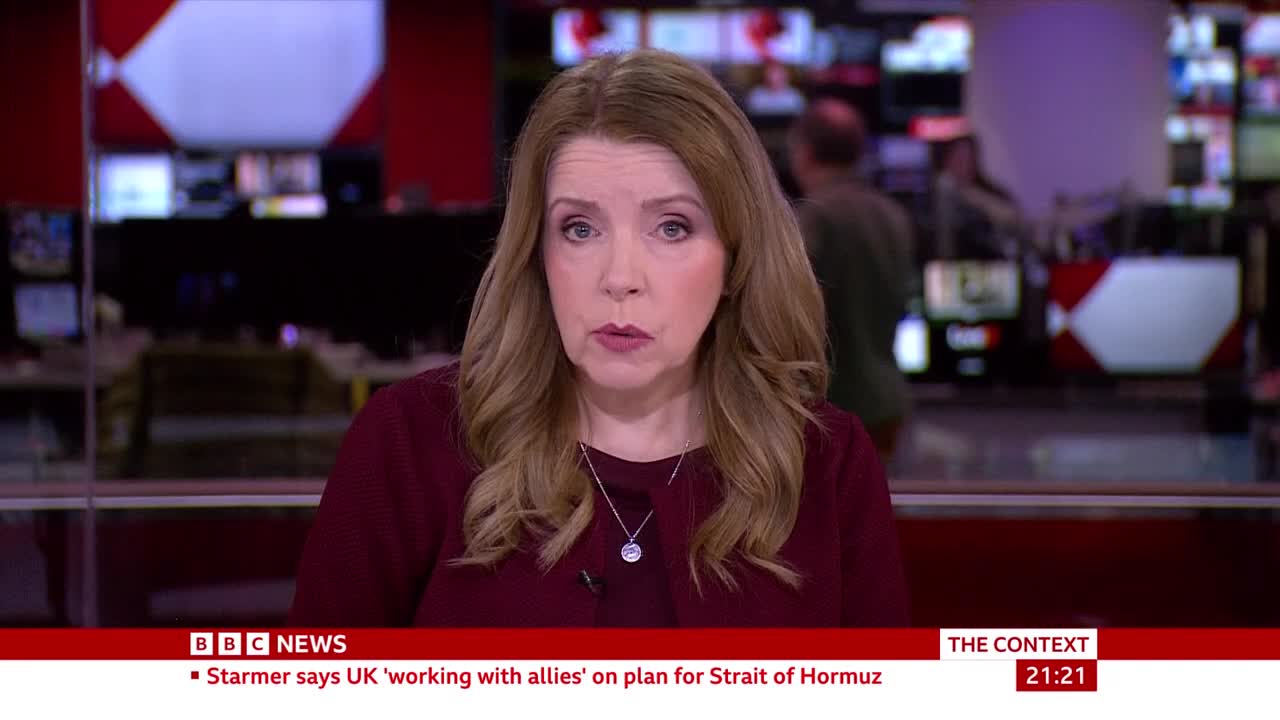 A woman with auburn hair, wearing a maroon top, speaks directly to me. Behind her, a busy BBC News studio hums with activity, screens displaying graphics and a few figures moving in the background.