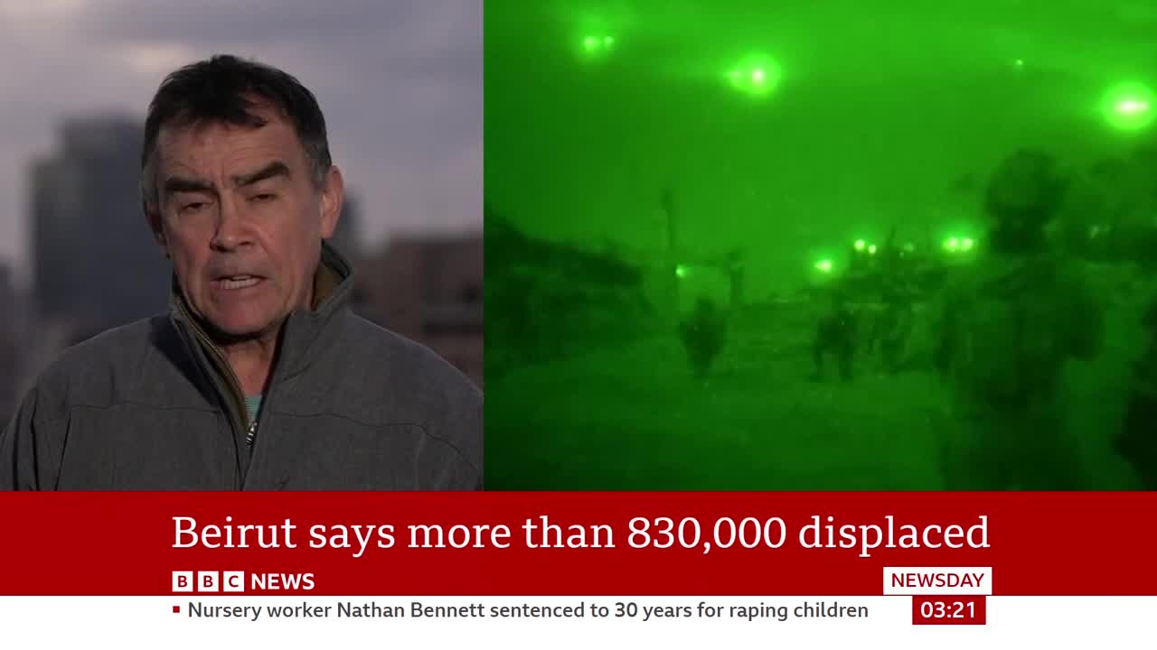 A man in a grey jacket stands to the left, speaking to the camera. To the right, figures move through a green, night-vision scene, illuminated by bright lights.