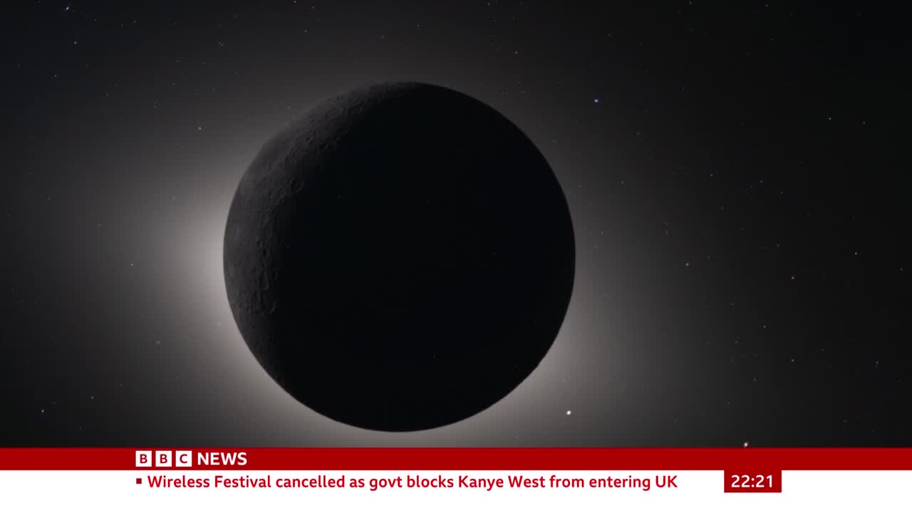 A dark sphere, the moon, is slowly passing in front of a bright, starry sky. A thin, glowing halo of light outlines its edge.