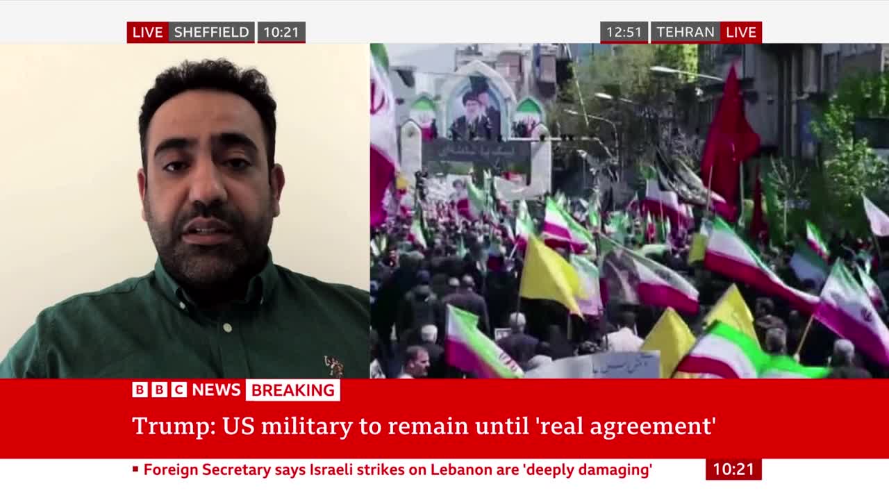 A crowd waves numerous flags, some green and white with red stripes, others solid red or yellow. The BBC News broadcast shows a split screen with a man speaking on the left and the demonstration on the right.