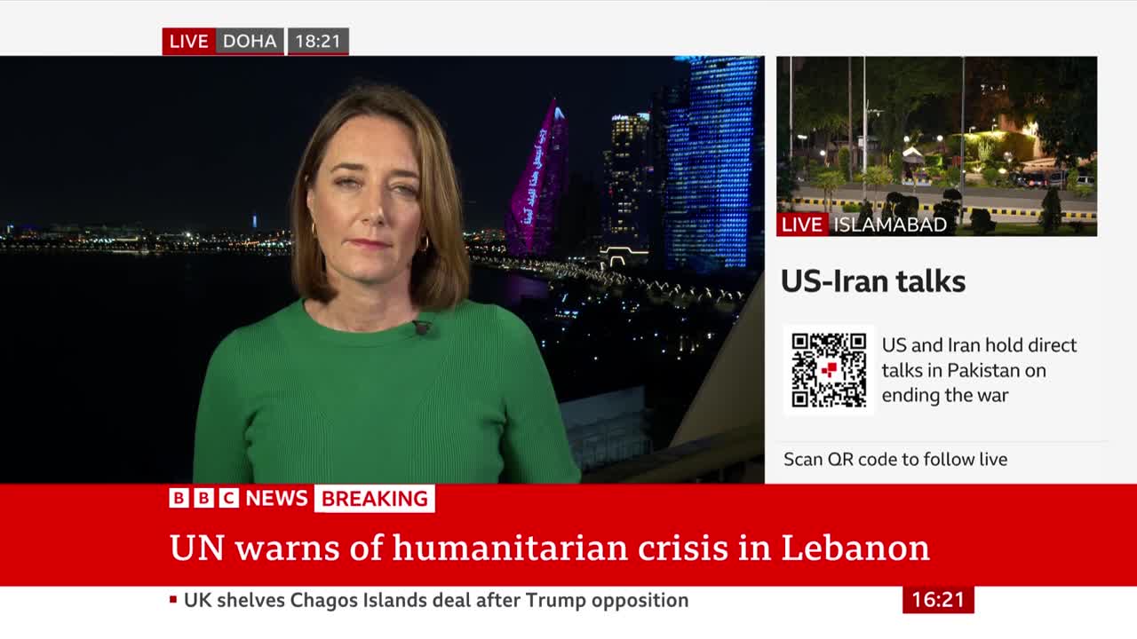 A woman in a green top stands before a city skyline at night.  The BBC News chyron below announces a UN warning of a humanitarian crisis in Lebanon.