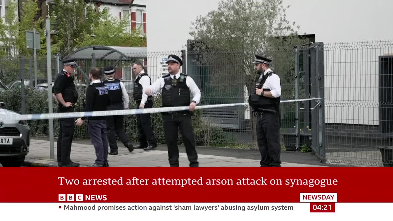 Several police officers stand by a synagogue, with tape cordoning off the entrance. A BBC News report states two people have been arrested following an attempted arson attack.
