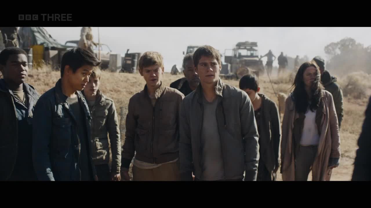 A group of young people, dressed in jackets and casual clothes, are walking towards the camera across a dry, open landscape. Behind them, several figures and vehicles are visible in the distance.
A group of young people, dressed in jackets and casual clothes, are walking towards the camera across a dry, open landscape. Behind them, several figures and vehicles are visible in the distance.