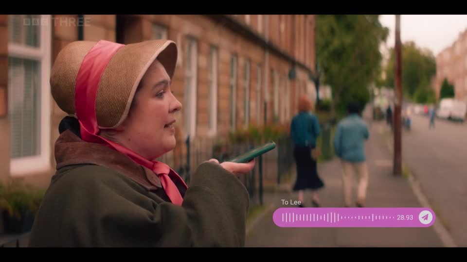 A woman in a bonnet holds out a green phone, a voice note playing. Two people walk away down a London street, their figures softened by the distance.