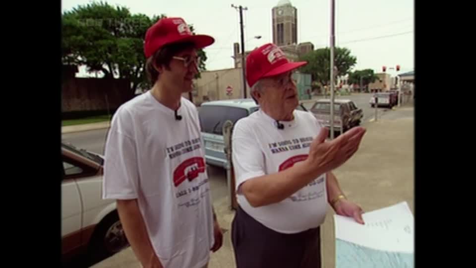 Two men in matching red caps and white t-shirts stand on a street, one gesturing with his hand. A BBC Three logo is visible in the corner, suggesting this is a segment from a UK television program.