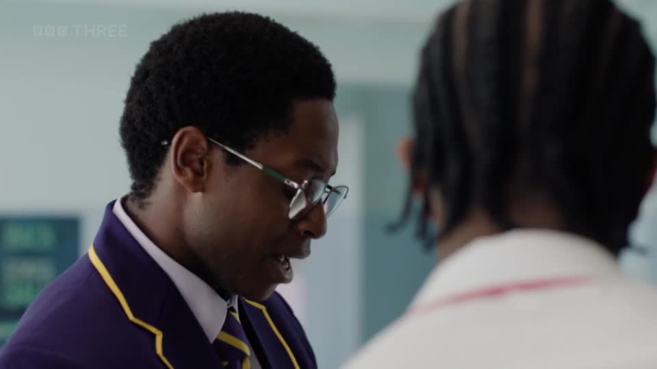 A young man in a purple blazer with yellow trim leans in, speaking intently. The BBC Three logo is visible in the corner, suggesting this is a scene from a UK production.