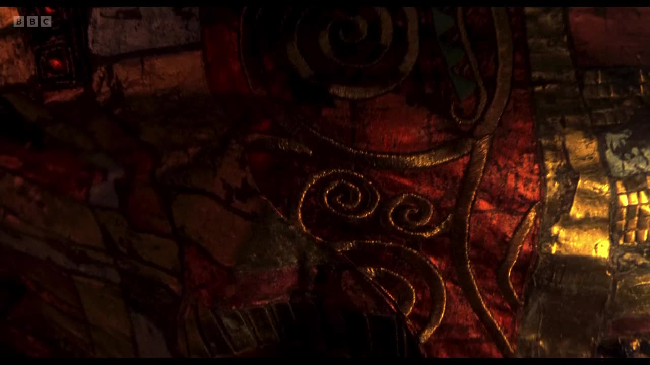 Intricate gold swirls adorn a deep red fabric, catching the light. The BBC Two logo is visible in the corner, hinting at a historical drama or a costume piece.
