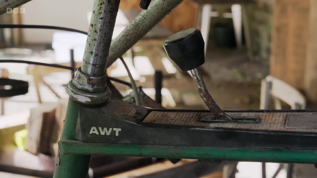 The rusty gear lever is held in place by a black knob, and it sits on a wooden surface. The AWT logo is visible on the green frame.
