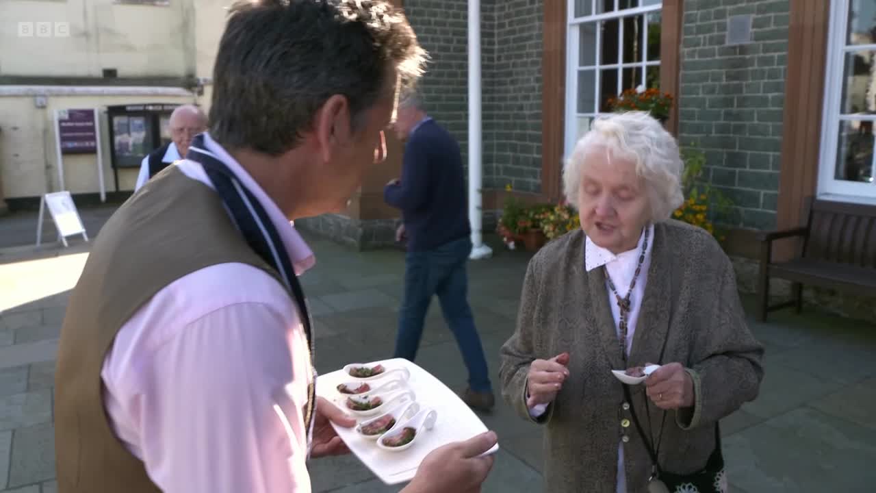 A man offers a plate of small, filled spoons to a woman. She holds her own spoon, seemingly tasting something, as a BBC Two crew films in the United Kingdom.
A man offers a plate of small, filled spoons to a woman. She holds her own spoon, seemingly tasting something, as a BBC Two crew films in the United Kingdom.