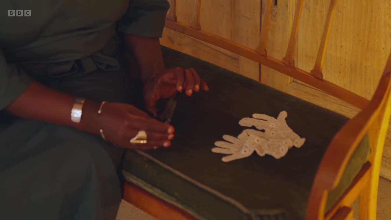 A woman in a dark green dress sits on a bench, her hands adorned with silver bracelets and a gold ring. Beside her, a delicate pair of white lace gloves rests on the dark upholstery.