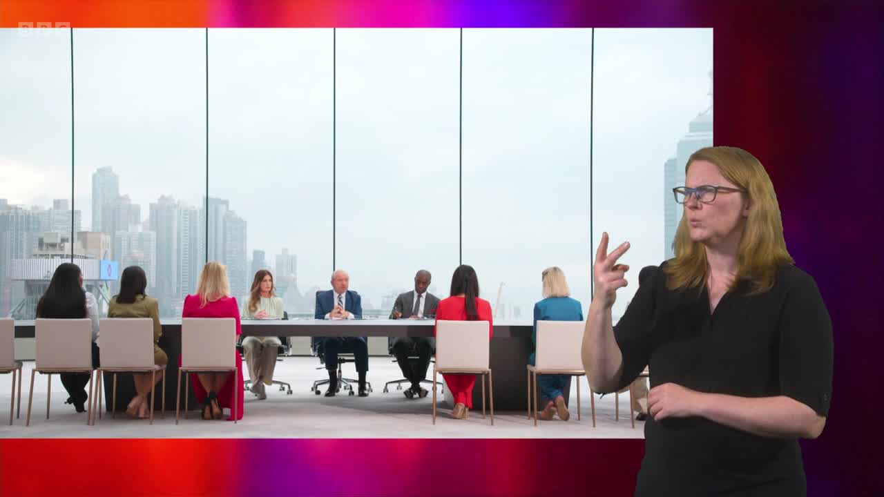 A woman signs on BBC Two, her hands moving as she interprets a boardroom discussion. In the background, a panel of people sit at a long table, facing a city skyline.