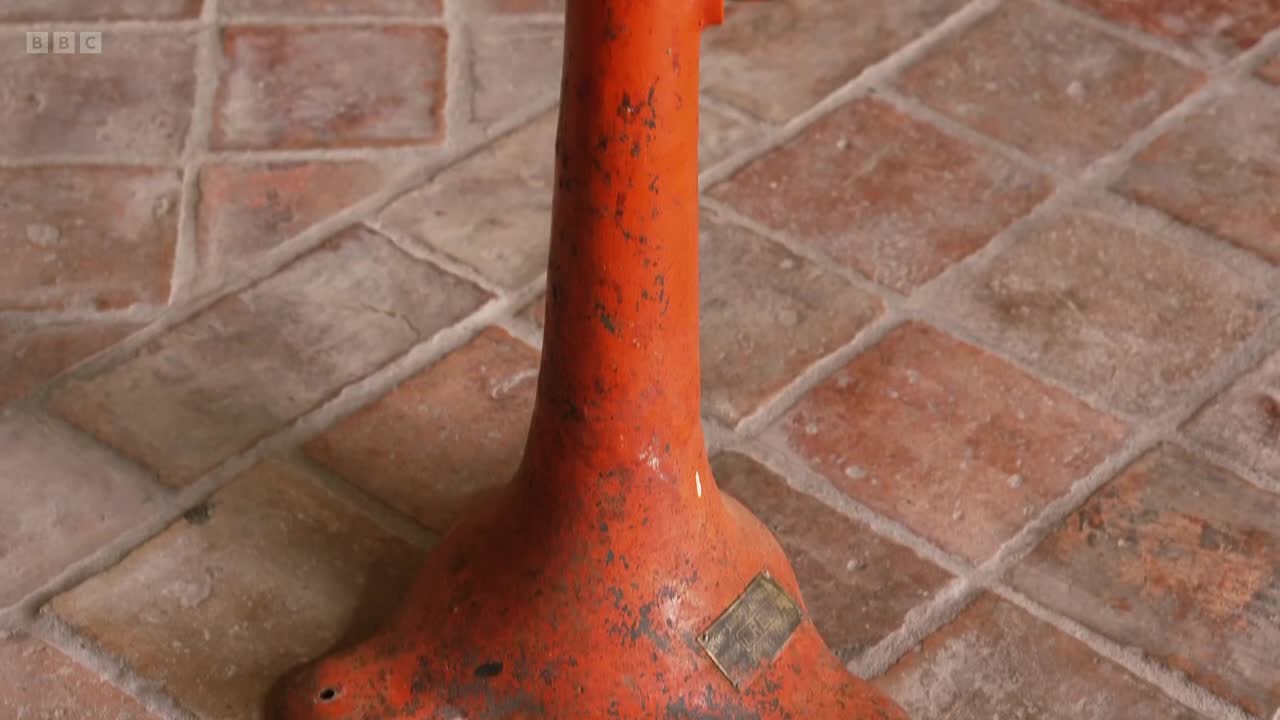 The camera pans across a worn, orange metal base on a tiled floor. A BBC Two logo appears in the corner.