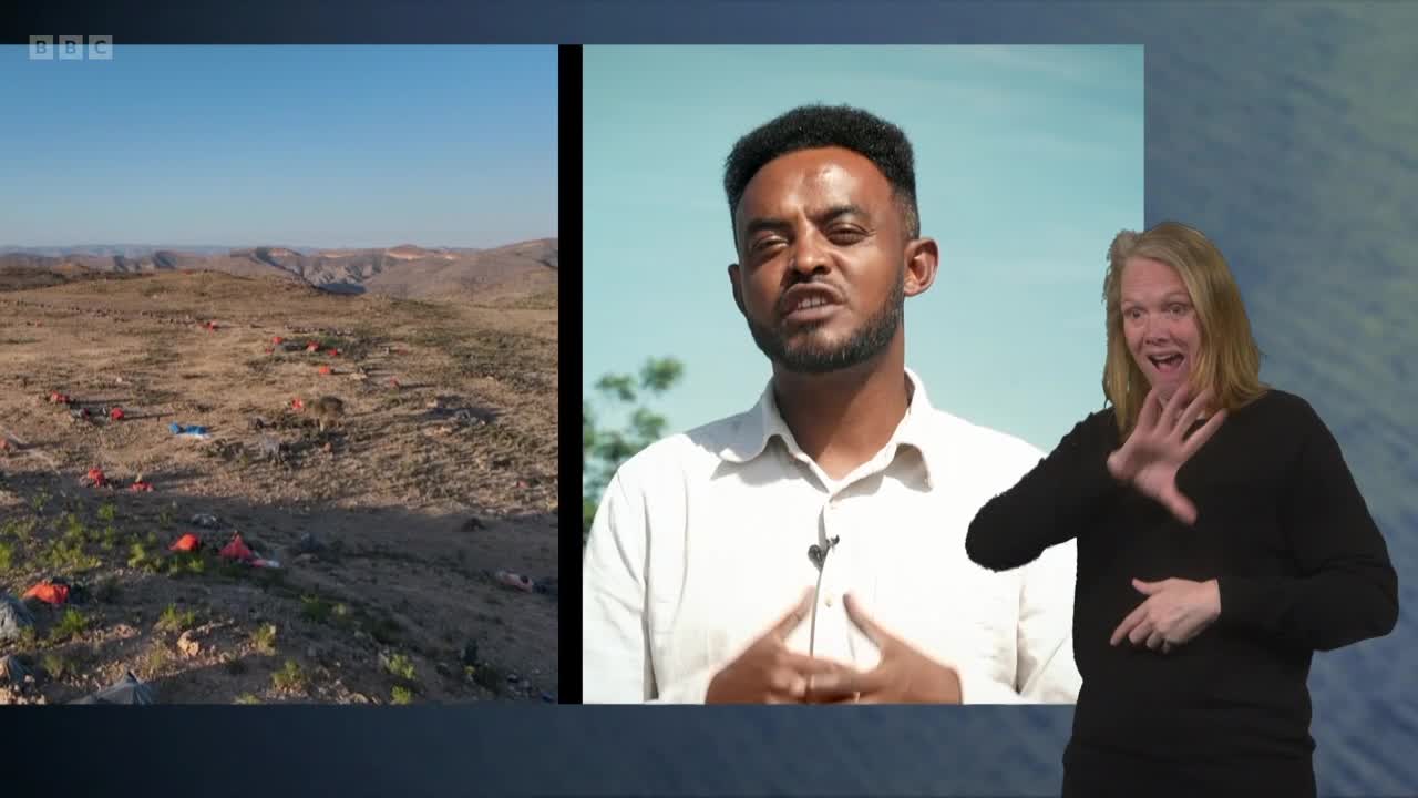 A wide shot shows a dusty, arid landscape dotted with numerous small, brightly colored tents. Beside it, a man speaks directly to the camera, while a woman in the foreground signs along.