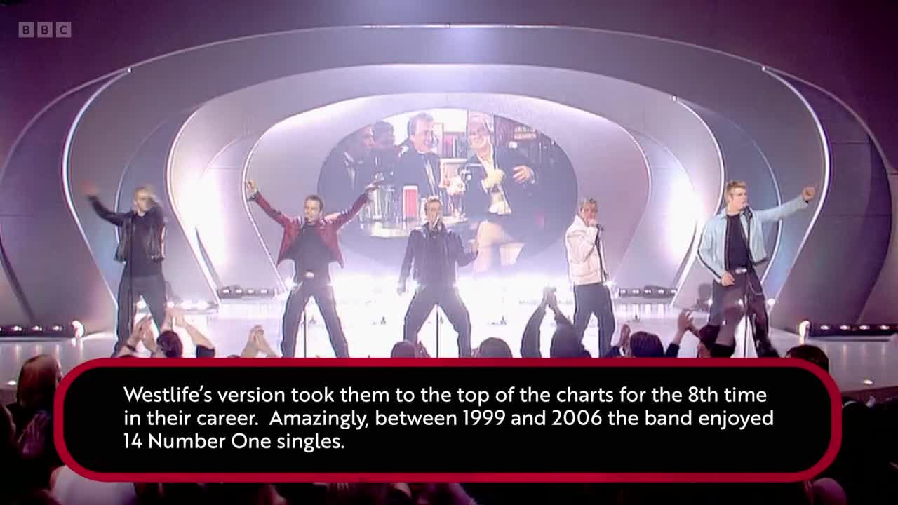 Five men in matching outfits are performing on a stage, their arms raised. The BBC Two logo is visible in the top left corner.