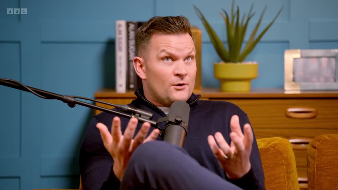 A man is speaking animatedly into a microphone, his hands gesturing to emphasize his words. This appears to be a segment from a BBC Two program, possibly a podcast recording.