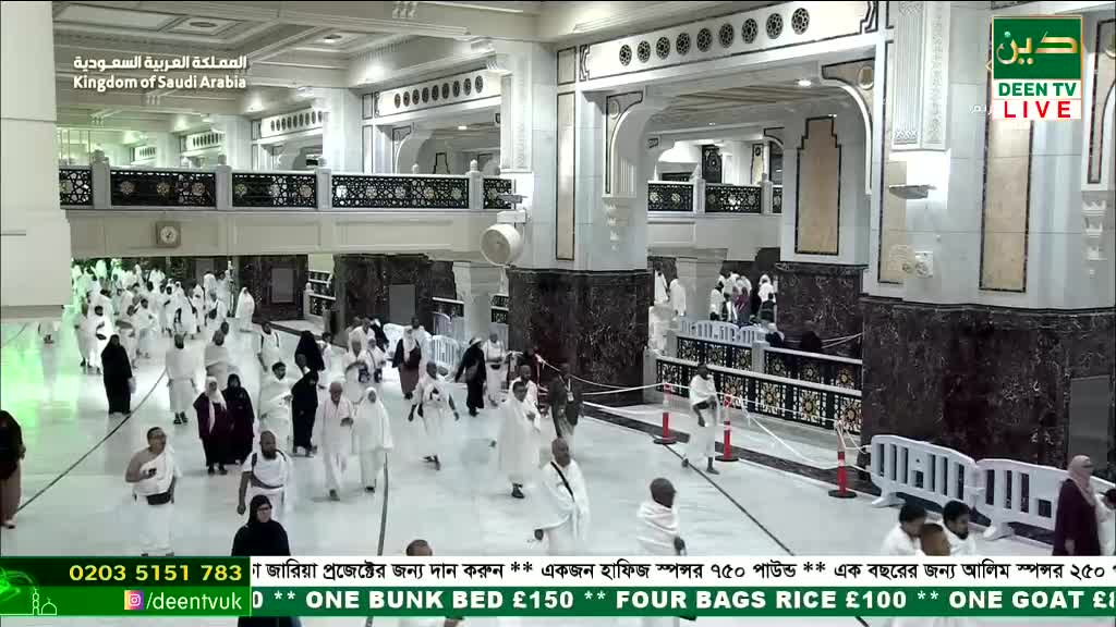 Pilgrims in white robes are moving through a vast, ornate hall. The Deen TV broadcast shows the scene live, with donation details scrolling across the bottom.
