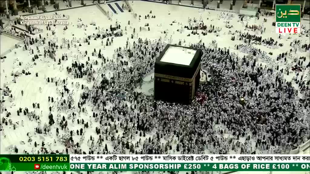 A dense crowd of people in white robes circles a large, black, cube-shaped structure. The scene is broadcast live on Deen TV, with donation information scrolling across the bottom.
