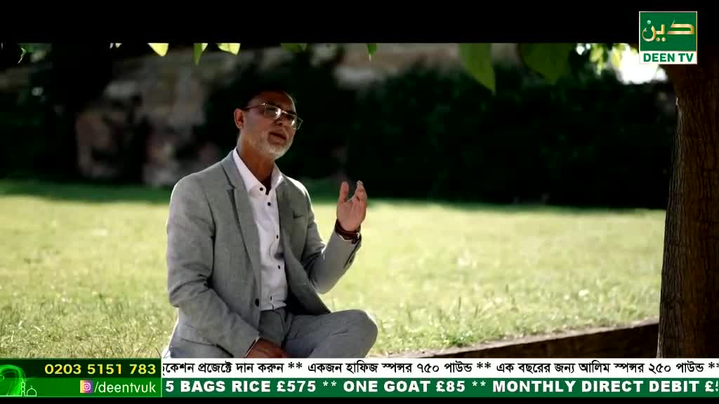 A man in a grey suit sits cross-legged on the grass, gesturing with his hand as he speaks. The Deen TV logo is visible, and the scene appears to be filmed outdoors in the United Kingdom.
