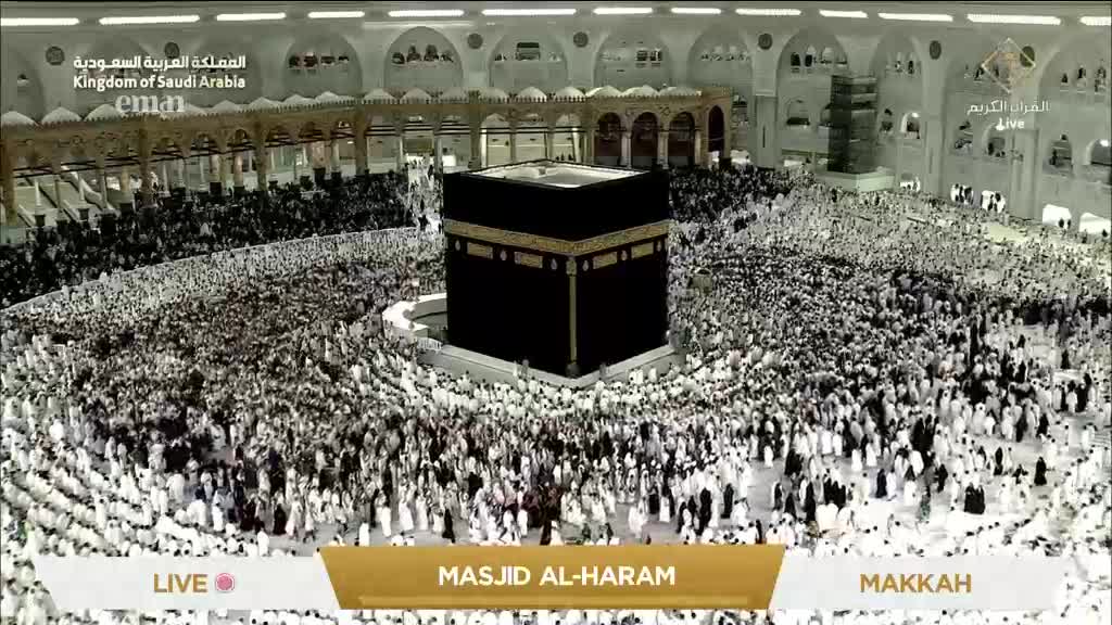 Thousands of people, mostly in white, are circling the black Kaaba, a central structure. The scene is being broadcast live from Masjid al-Haram in Makkah, as seen on Eman Channel.
