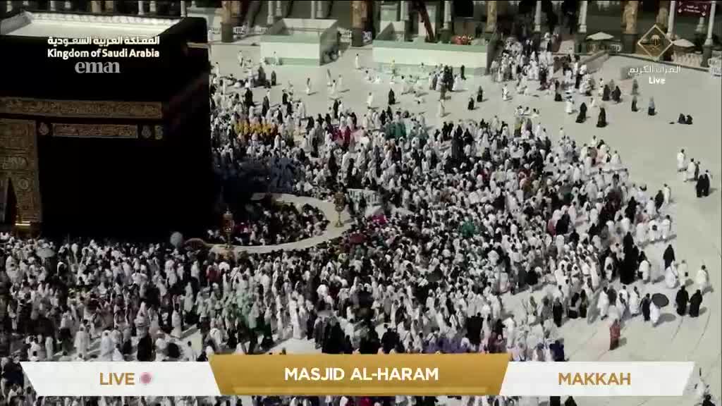A sea of white-clad figures flows around the black cube of the Kaaba. The scene, broadcast live on Eman Channel, shows the bustling activity in Masjid al-Haram, Makkah.
