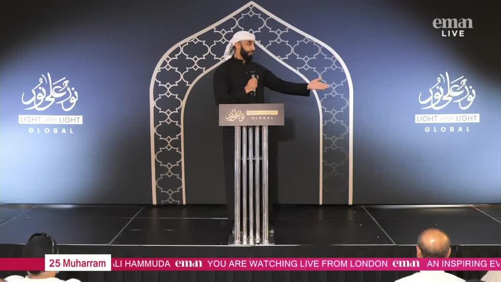 A man in a black outfit and white head covering gestures with his right hand while speaking into a microphone. The Eman Channel broadcast is live from London, with a backdrop featuring Arabic calligraphy and a decorative arch.

