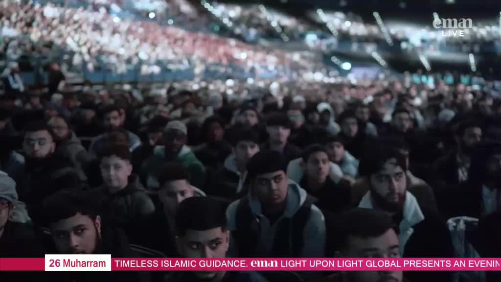 A large crowd of people, mostly young men, are seated in an arena, all facing the same direction. The Eman Channel logo is visible, suggesting a live broadcast from the United Kingdom.
