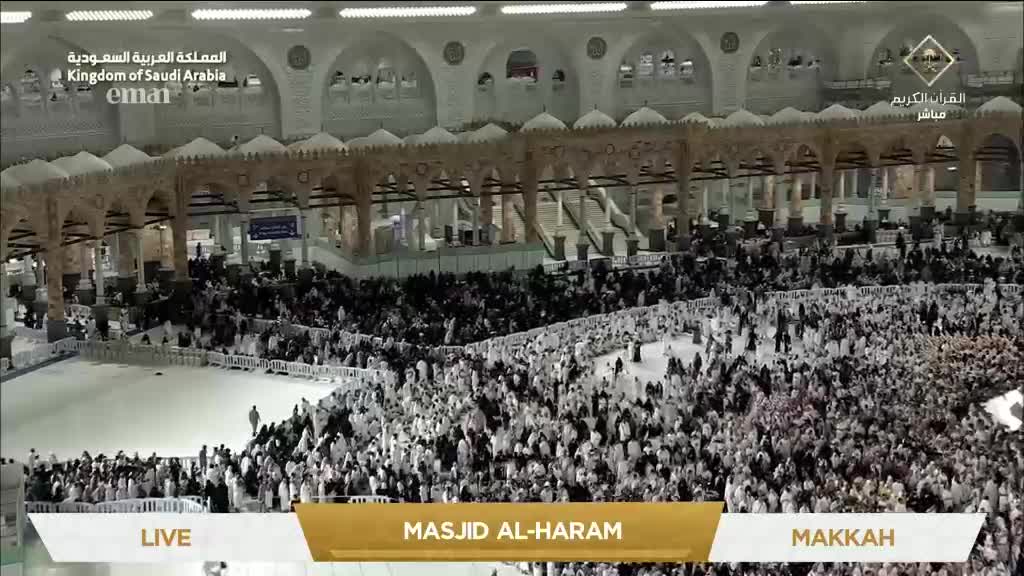 Thousands of people, mostly in white, are packed together, moving slowly across the vast marble floor. Overhead, the ornate architecture of the Masjid al-Haram provides a stark contrast to the dense crowd below, broadcast live on Eman Channel.
