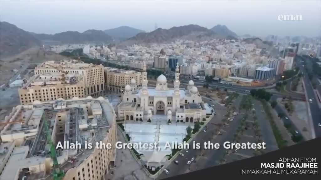 A large mosque with multiple minarets and domes dominates the foreground, surrounded by a sprawling city. The words "Allah is the Greatest" appear on the screen, likely as part of the adhan broadcast on the Eman Channel.
