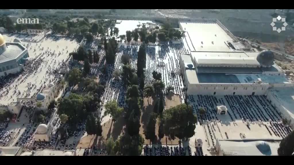 Hundreds of people are arranged in neat rows, facing the same direction, as if in prayer. The scene is being broadcast on Eman Channel, a United Kingdom-based media outlet.
