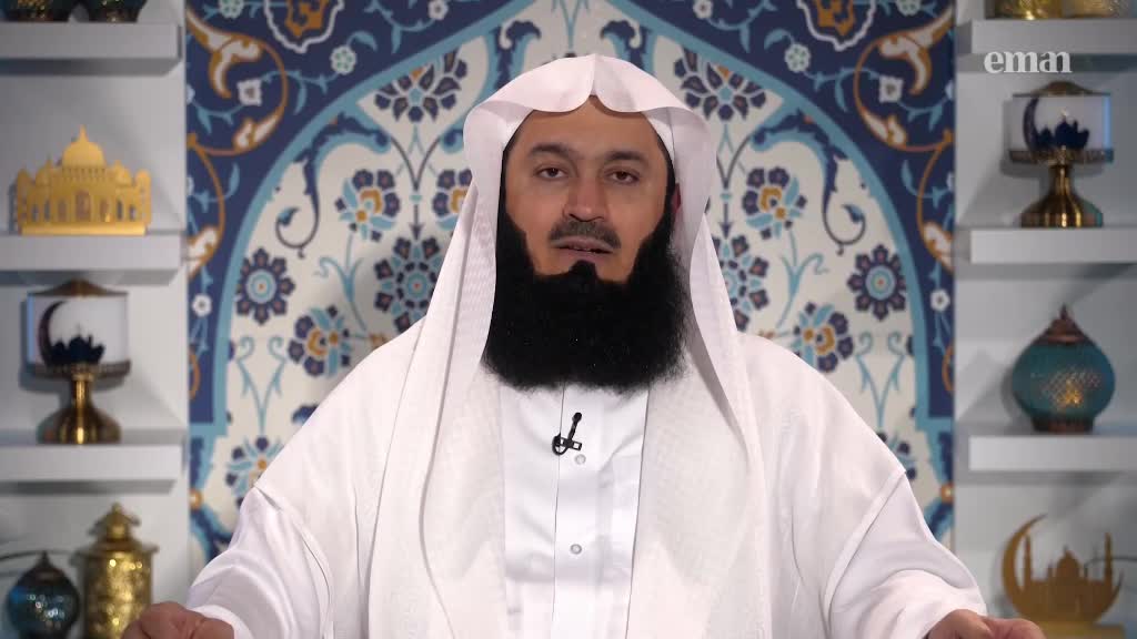 A man in white robes speaks directly to the camera, a small microphone clipped to his collar. Behind him, the Eman Channel logo is visible, and the set is decorated with shelves holding ornate objects.
