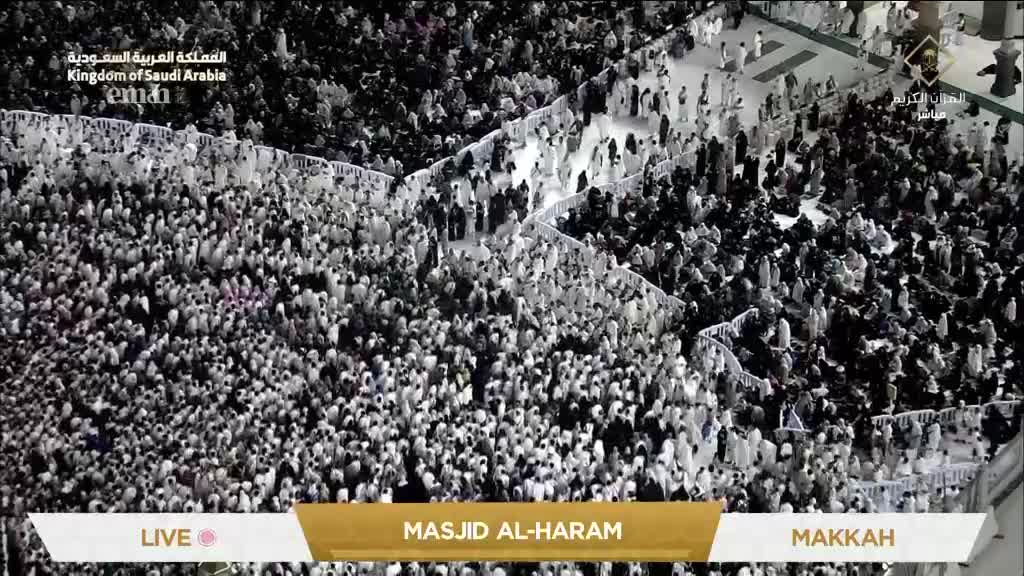 A vast crowd, mostly in white, flows through the Masjid al-Haram in Mecca, as seen live on Eman Channel. The movement is constant, a sea of people filling the space.
