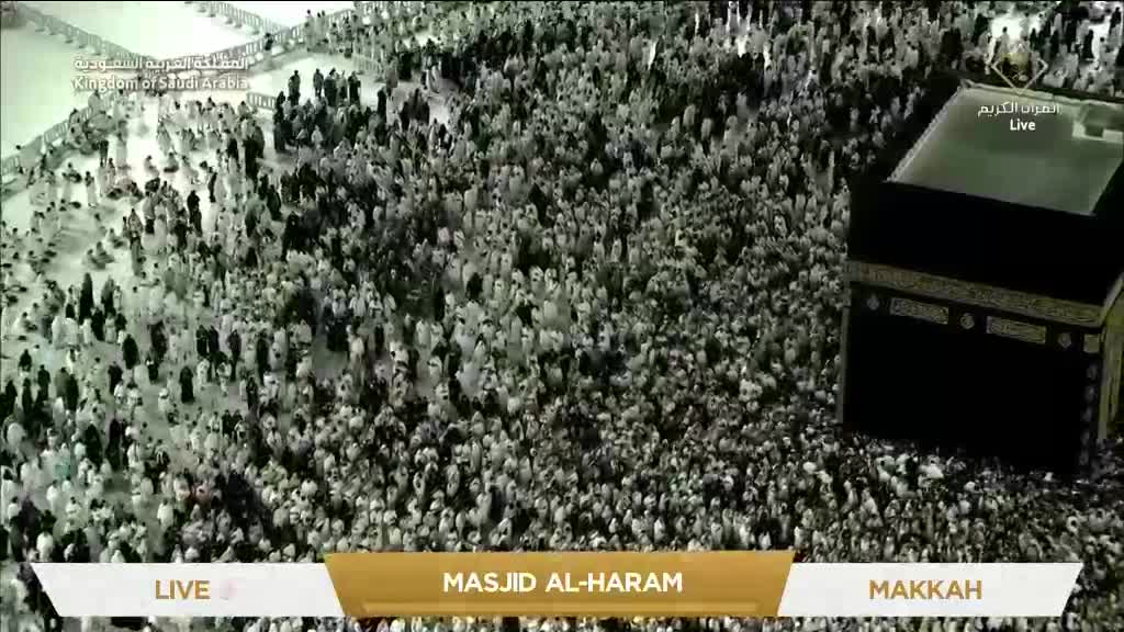 A sea of people in white garments surrounds the black cube, all moving slowly. The live broadcast from Masjid Al-Haram is showing the scene in Mecca.
