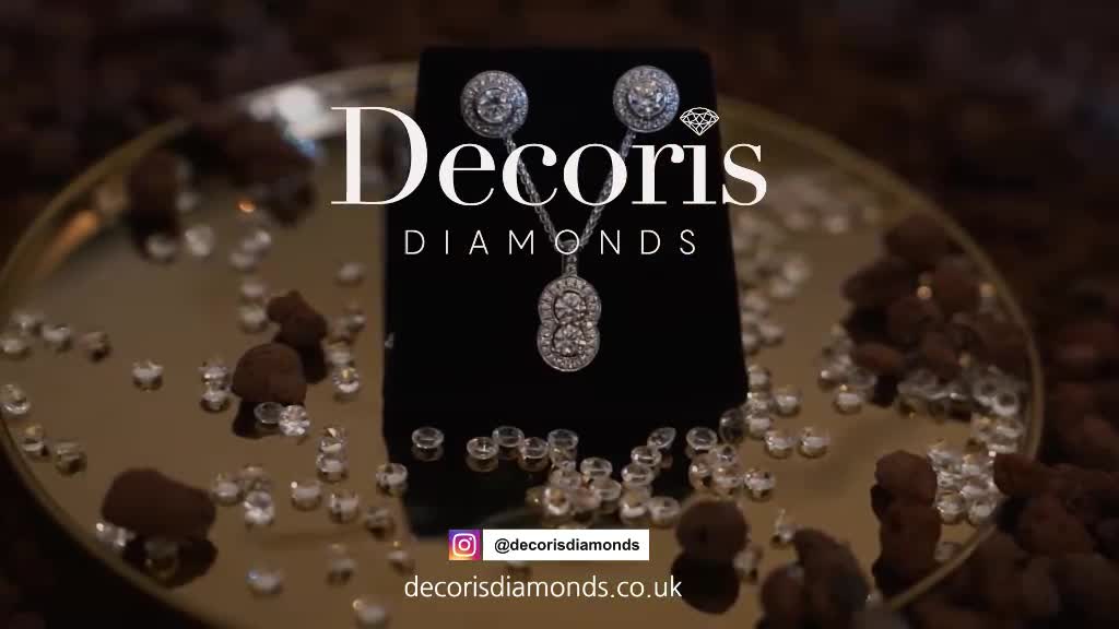 A diamond necklace and earrings set sits on a black velvet stand, surrounded by scattered crystals and what look like chocolate truffles. The jewelry sparkles under the light, catching the eye against the dark background.
