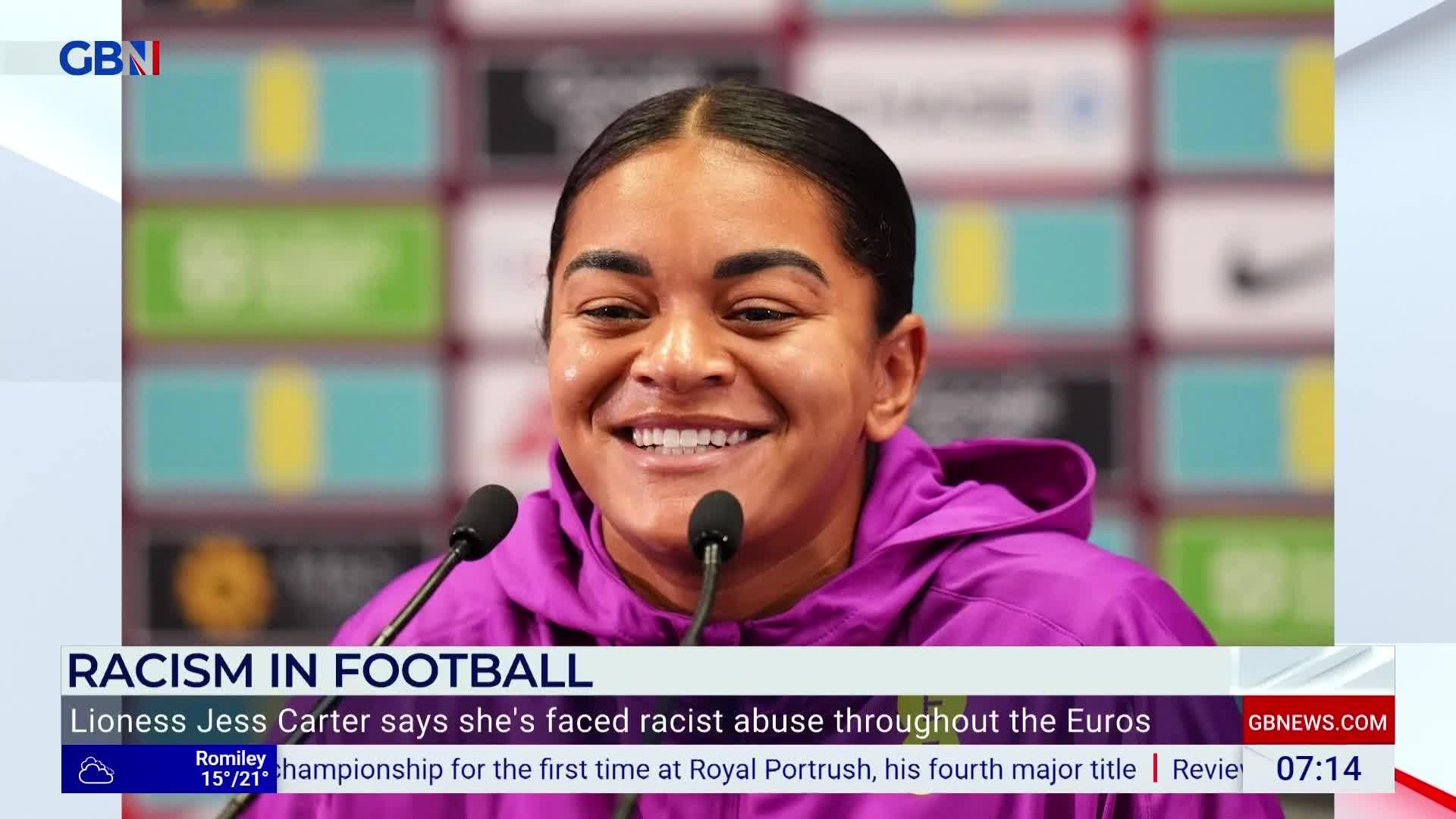 A woman in a purple hoodie smiles brightly at the microphones in front of her. The GB News graphic at the bottom of the screen indicates the topic is racism in football, with a headline about Lioness Jess Carter.
