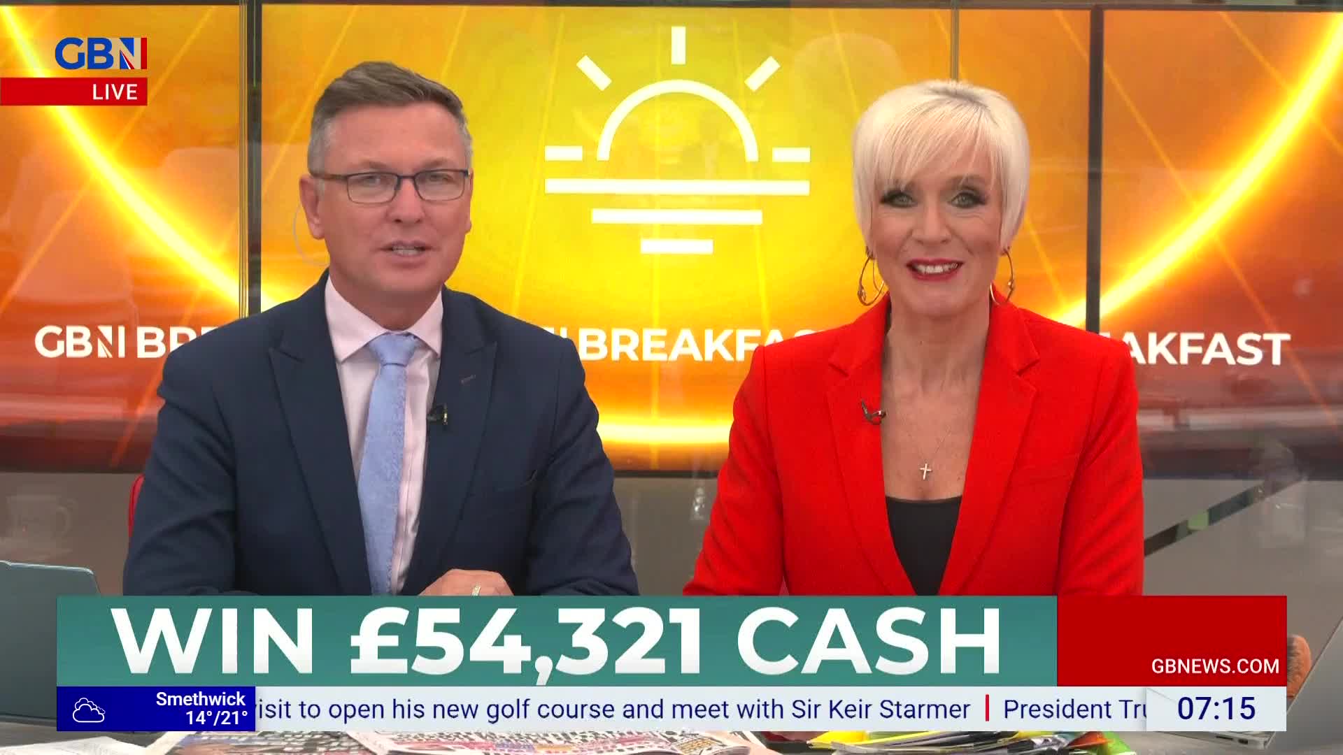 Two presenters from GB News are smiling directly at the camera, the man in a blue suit and the woman in a bright red jacket. Beneath them, a graphic advertises a cash giveaway.
