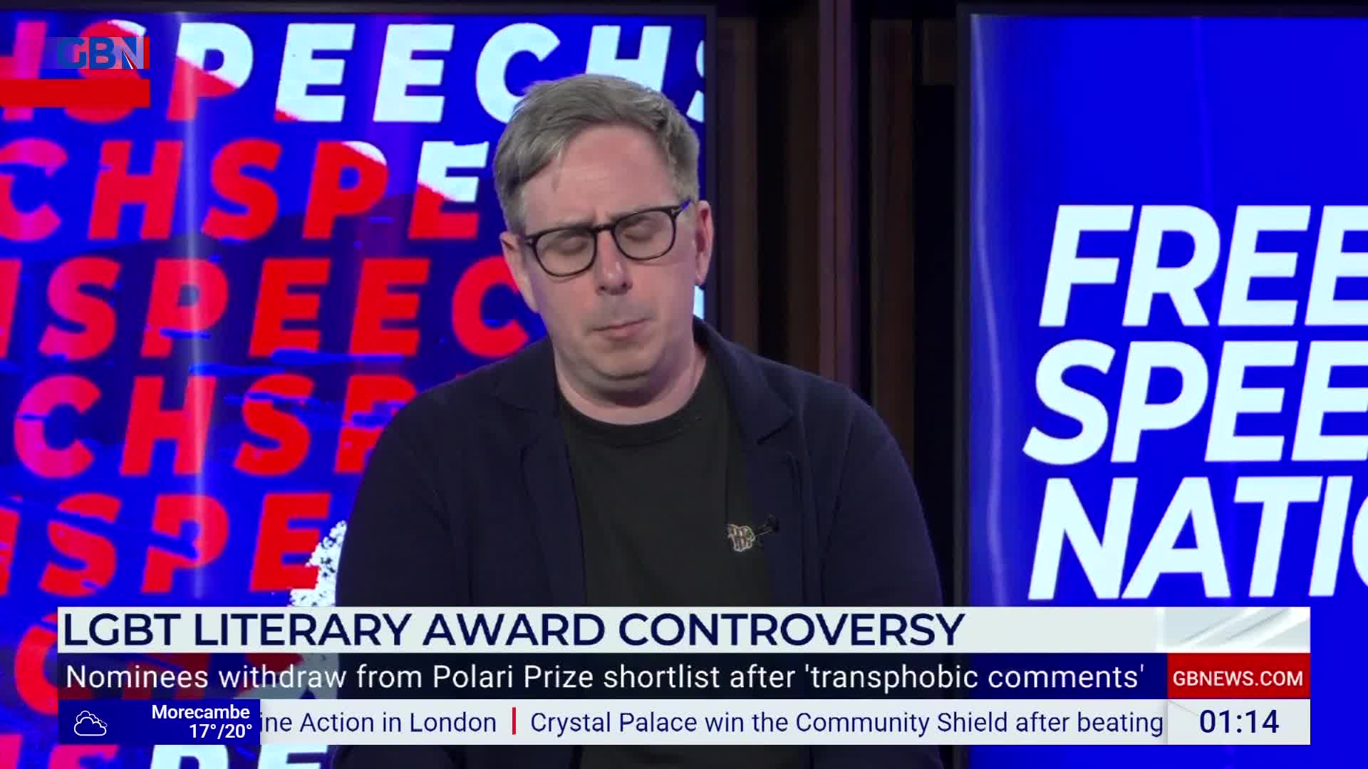 A man in glasses is speaking on a GB News set, looking down with a serious expression. Behind him, the words "FREE SPEECH NATION" are visible on a blue backdrop.
