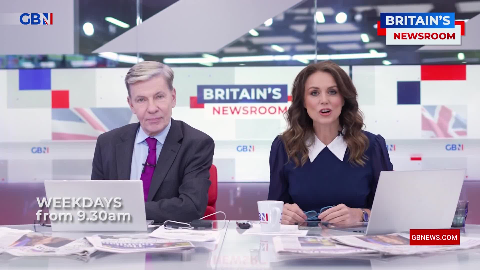 Two presenters sit at a desk, facing the camera, with the "Britain's Newsroom" logo visible overhead. The woman is speaking, while the man looks on, both in a studio setting for GB News in the United Kingdom.
