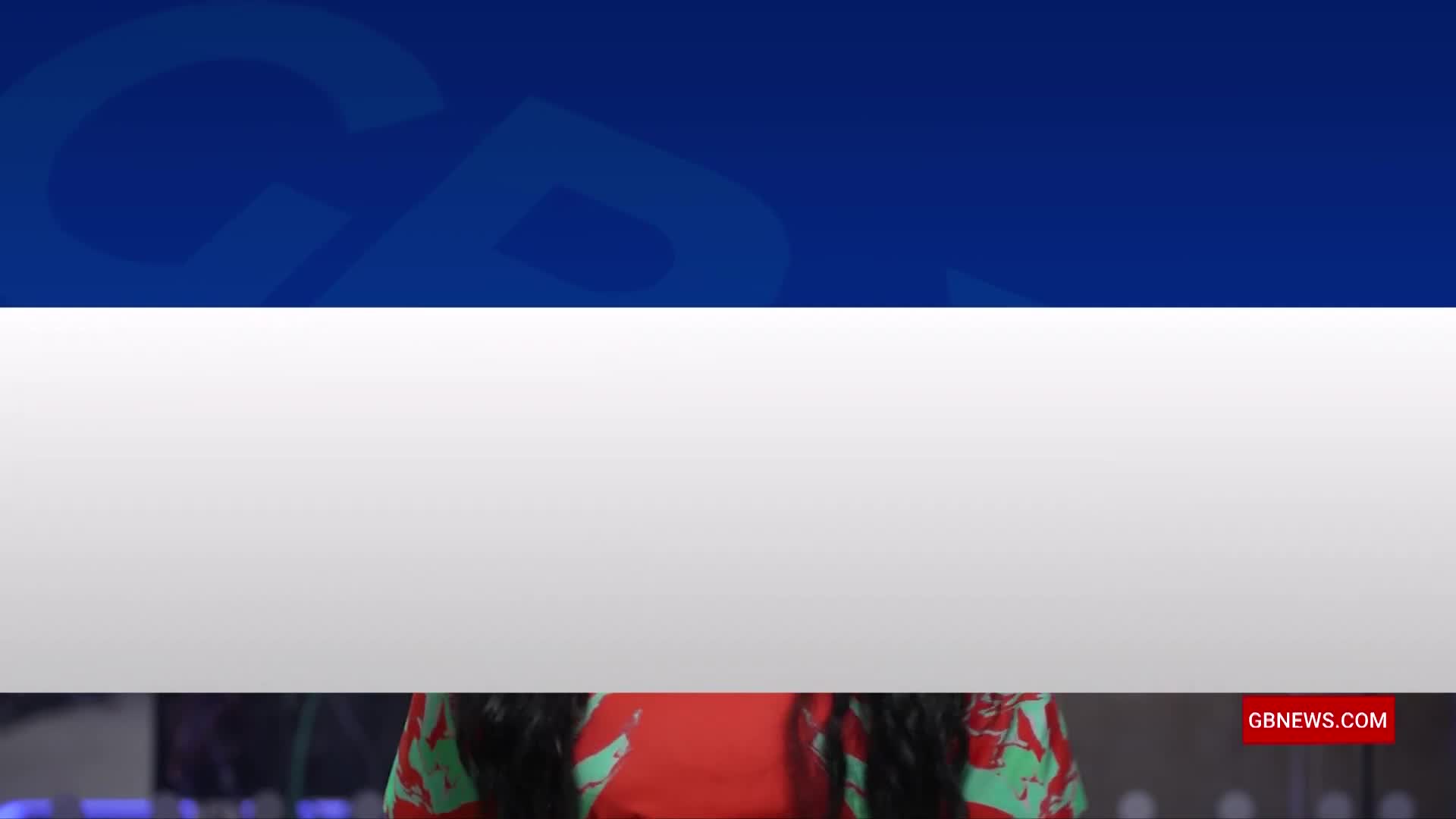 A red and green patterned top is visible below a blue and white background, with a GB News logo in the corner. The top half of the screen is dominated by the channel's branding.
