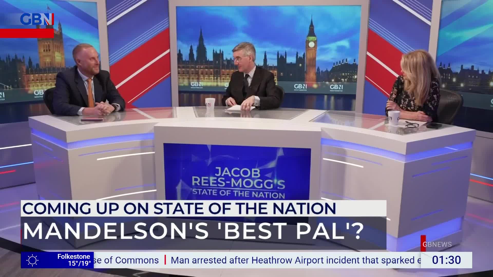Three people sit at a desk on a GB News set, ready for a segment on Jacob Rees-Mogg's "State of the Nation." The backdrop features images of the Houses of Parliament in the United Kingdom.
