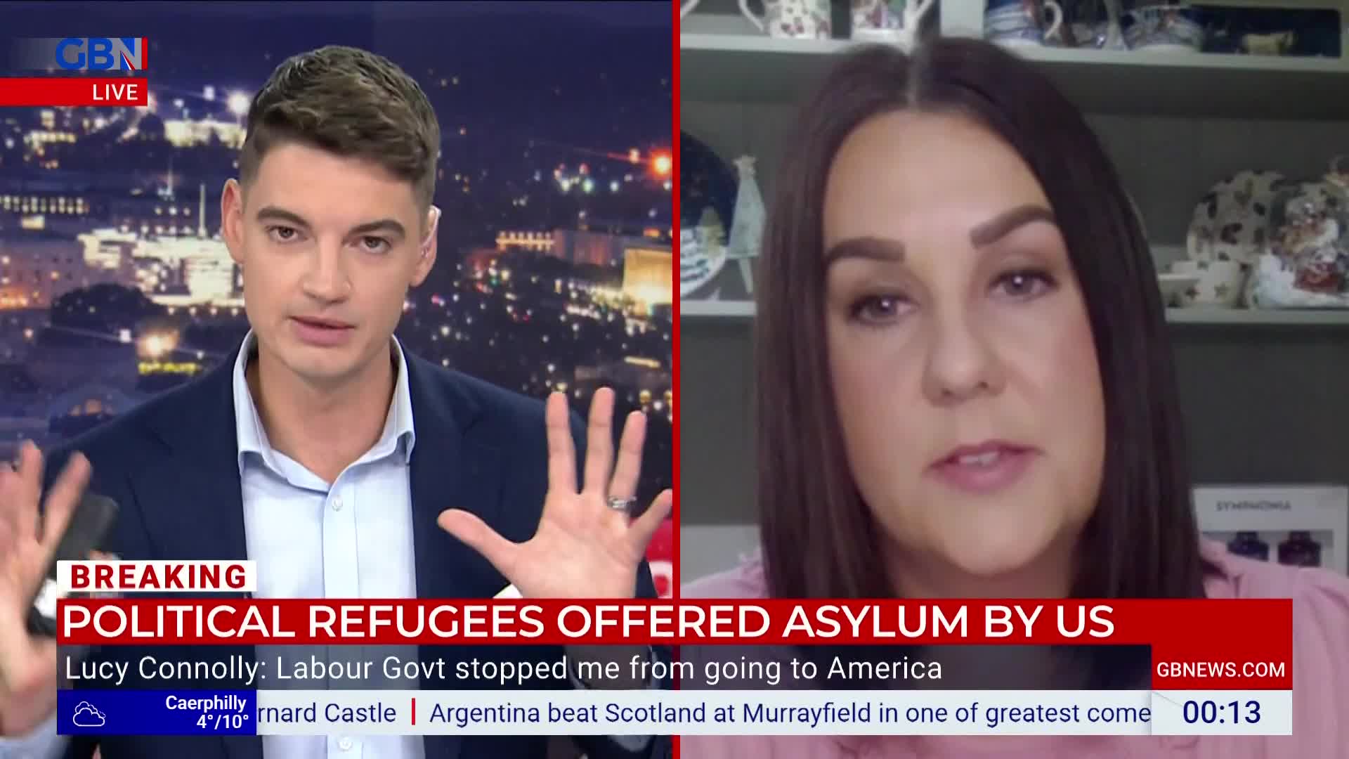 A man in a navy suit gestures with both hands as he speaks on GB News, his face lit by studio lights. On the right, a woman in a pink top talks, framed by a shelf with teacups.
