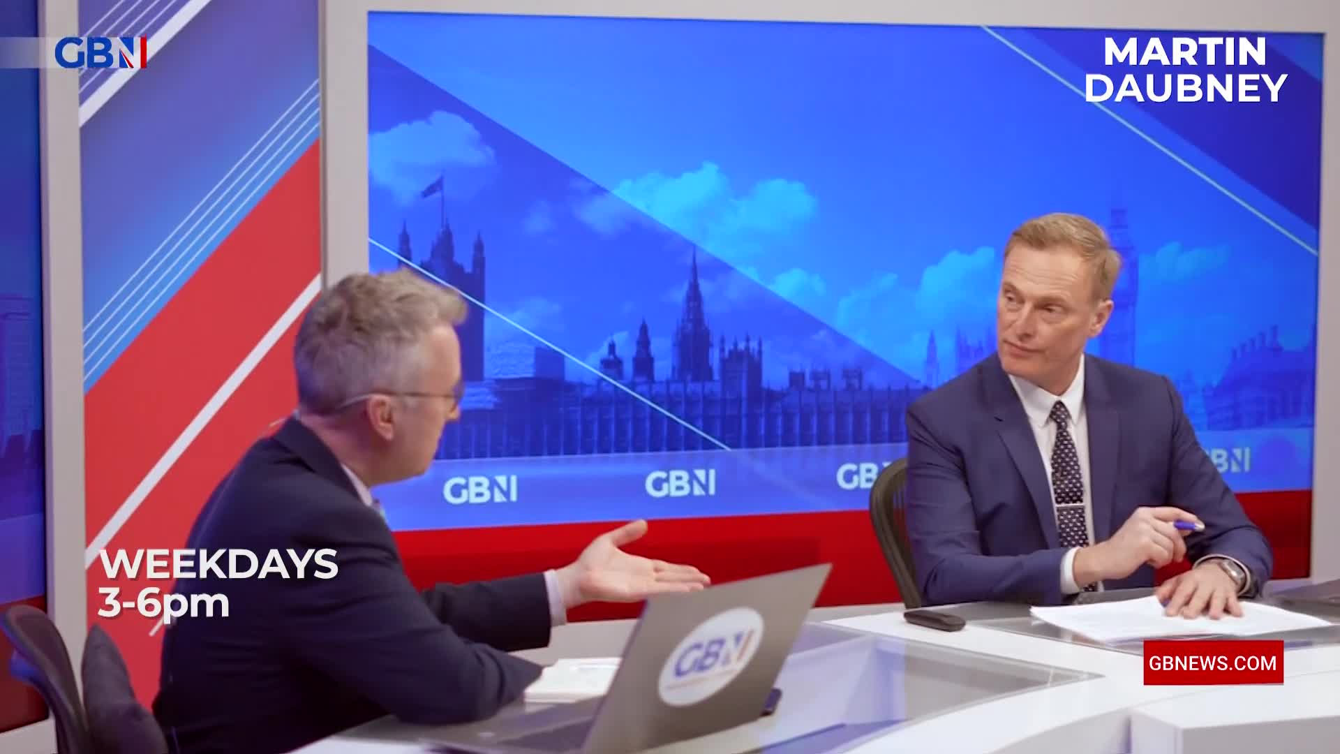 At a desk, a man in a suit gestures with his hand as he speaks. Across from him, another man in a suit listens intently, the backdrop showing the Houses of Parliament and the GB News logo.
At a desk, a man in a suit gestures with his hand as he speaks. Across from him, another man in a suit listens intently, the backdrop showing the Houses of Parliament and the GB News logo.