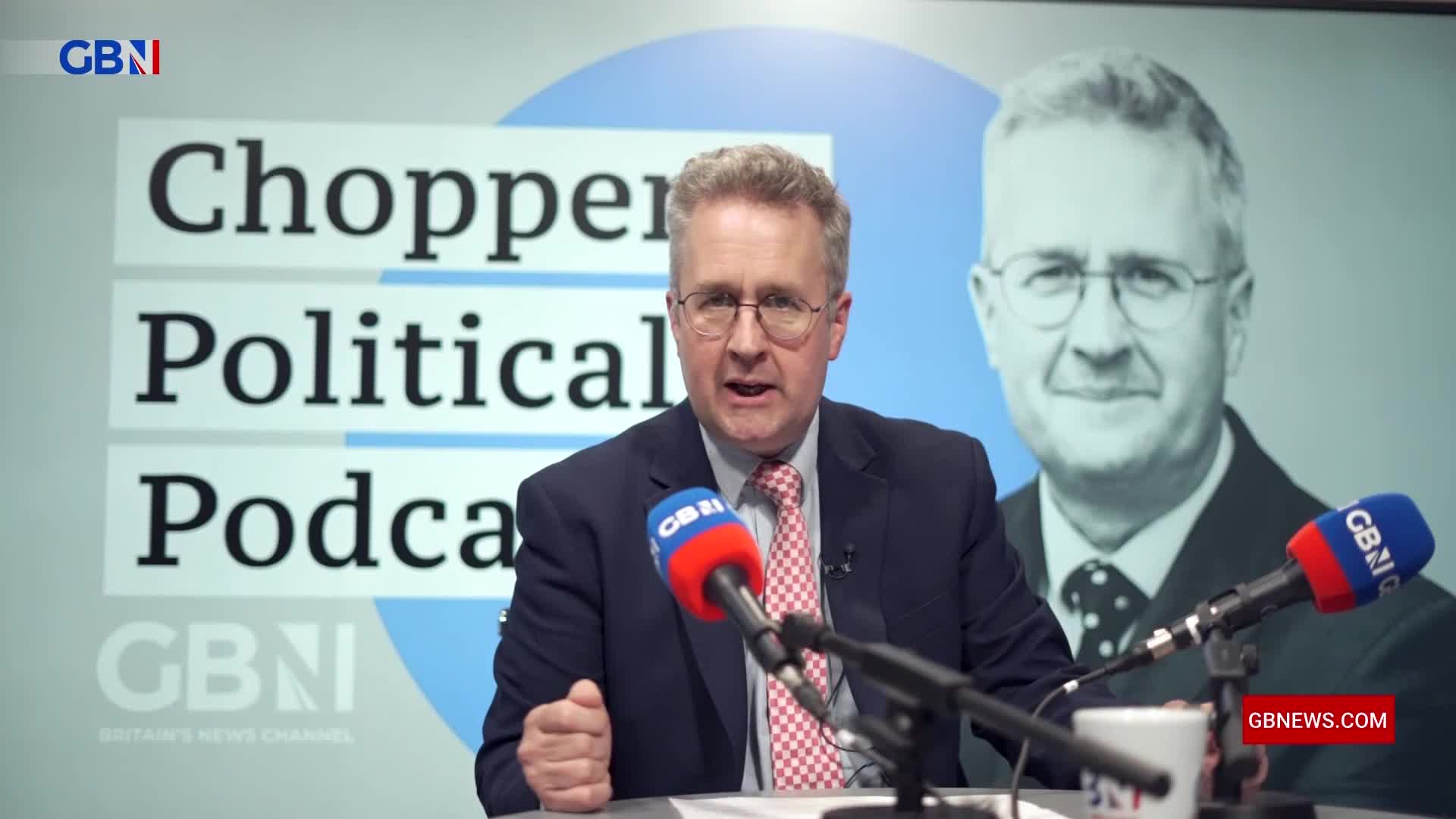A man in a suit and tie, speaking into two microphones, is the focus of the GB News "Chopper's Political Podcast." Behind him, a larger image of another man in a suit is visible on the screen.
A man in a suit and tie, speaking into two microphones, is the focus of the GB News "Chopper's Political Podcast." Behind him, a larger image of another man in a suit is visible on the screen.
