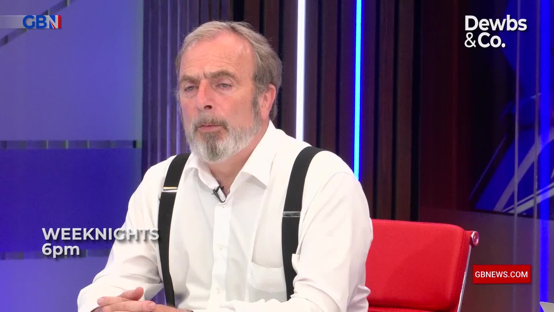 A man with a grey beard, wearing a white shirt and black suspenders, sits on a red chair. The GB News logo is visible in the corner, and the text "WEEKnights 6pm" appears on the screen.