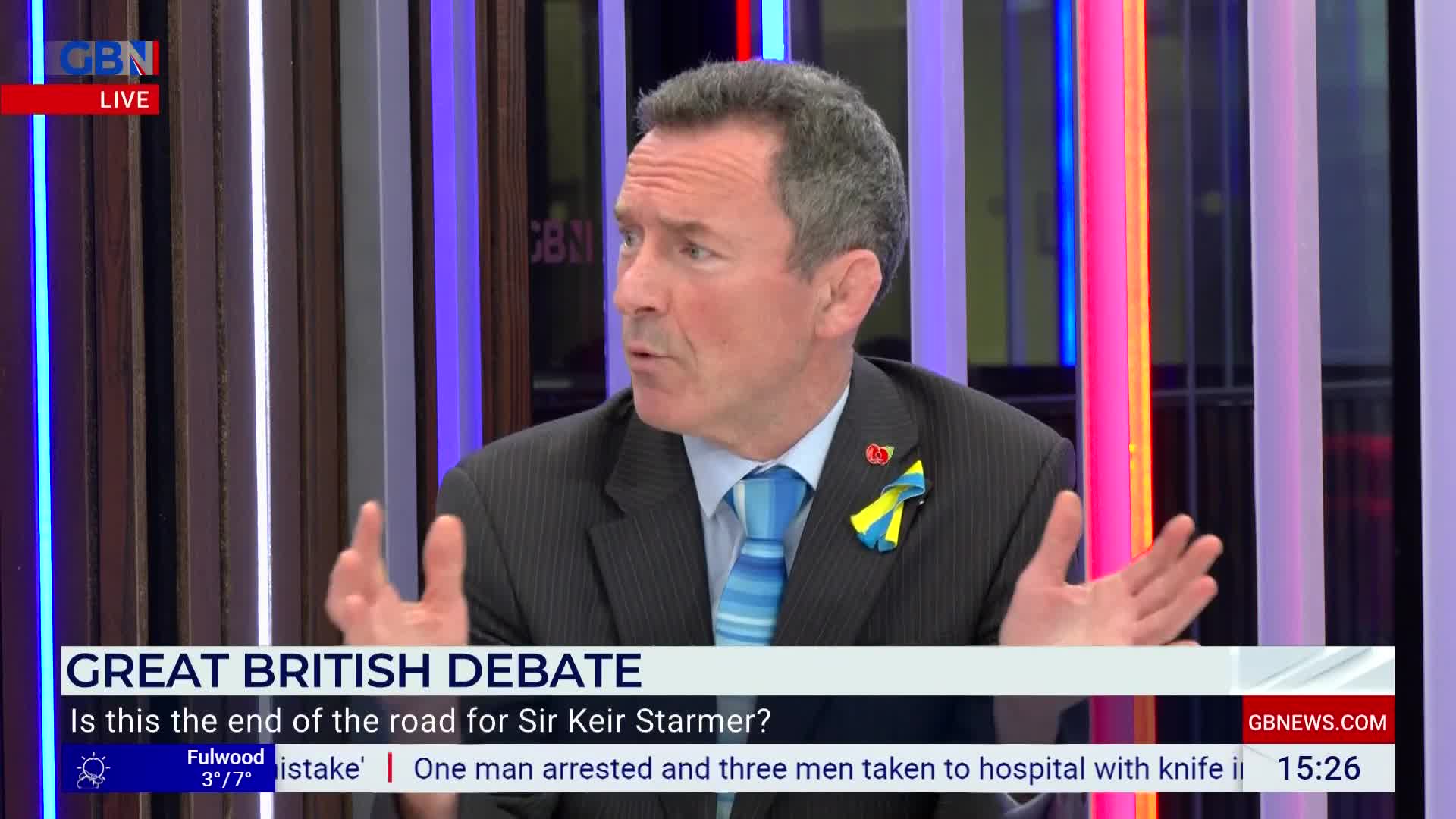 A man in a suit gestures with both hands while speaking on a GB News segment. The screen displays "GREAT BRITISH DEBATE" and a question about Sir Keir Starmer.