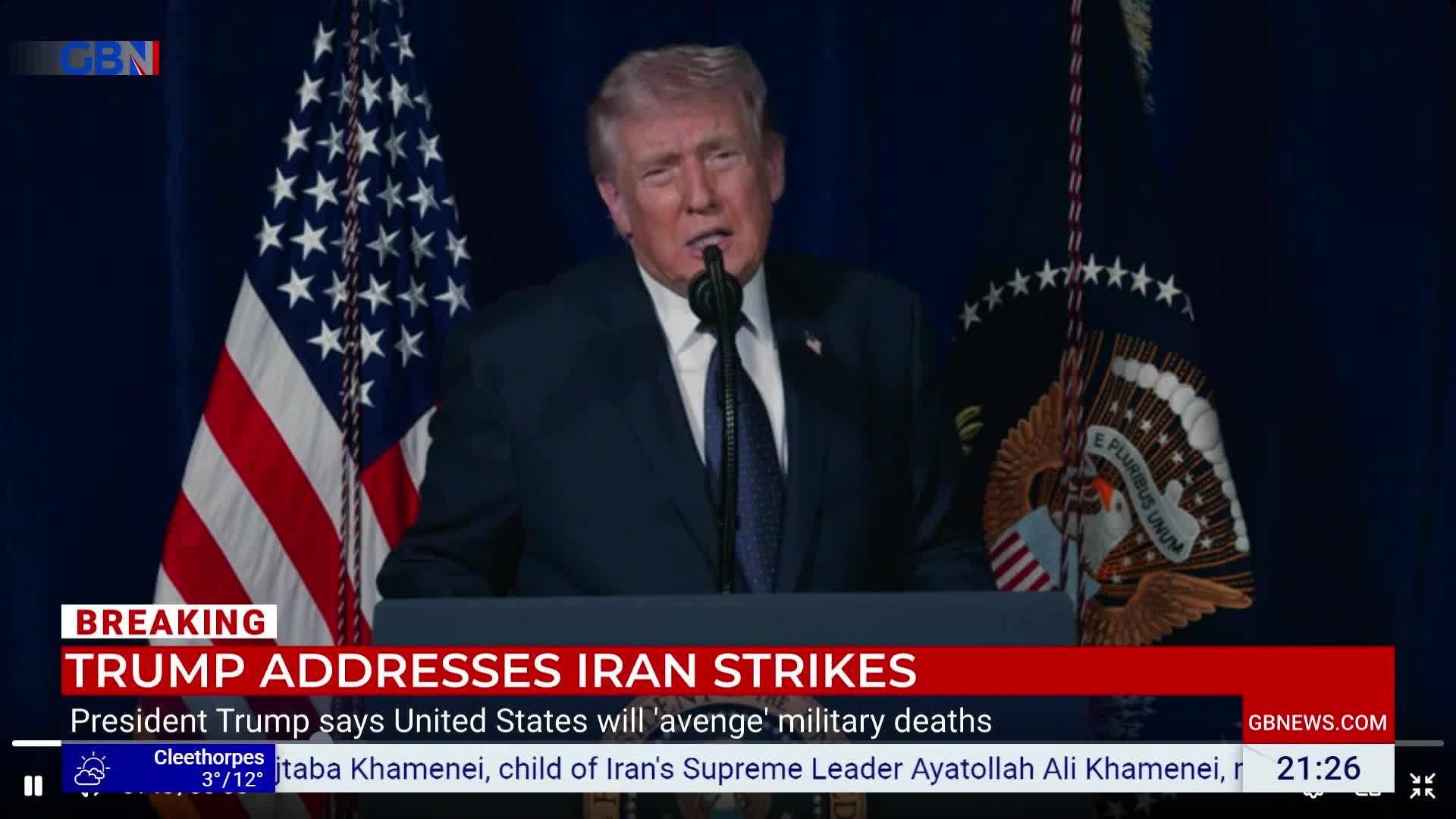 Donald Trump stands at a podium, speaking into a microphone. The American flag hangs behind him, and a GB News chyron scrolls below.
