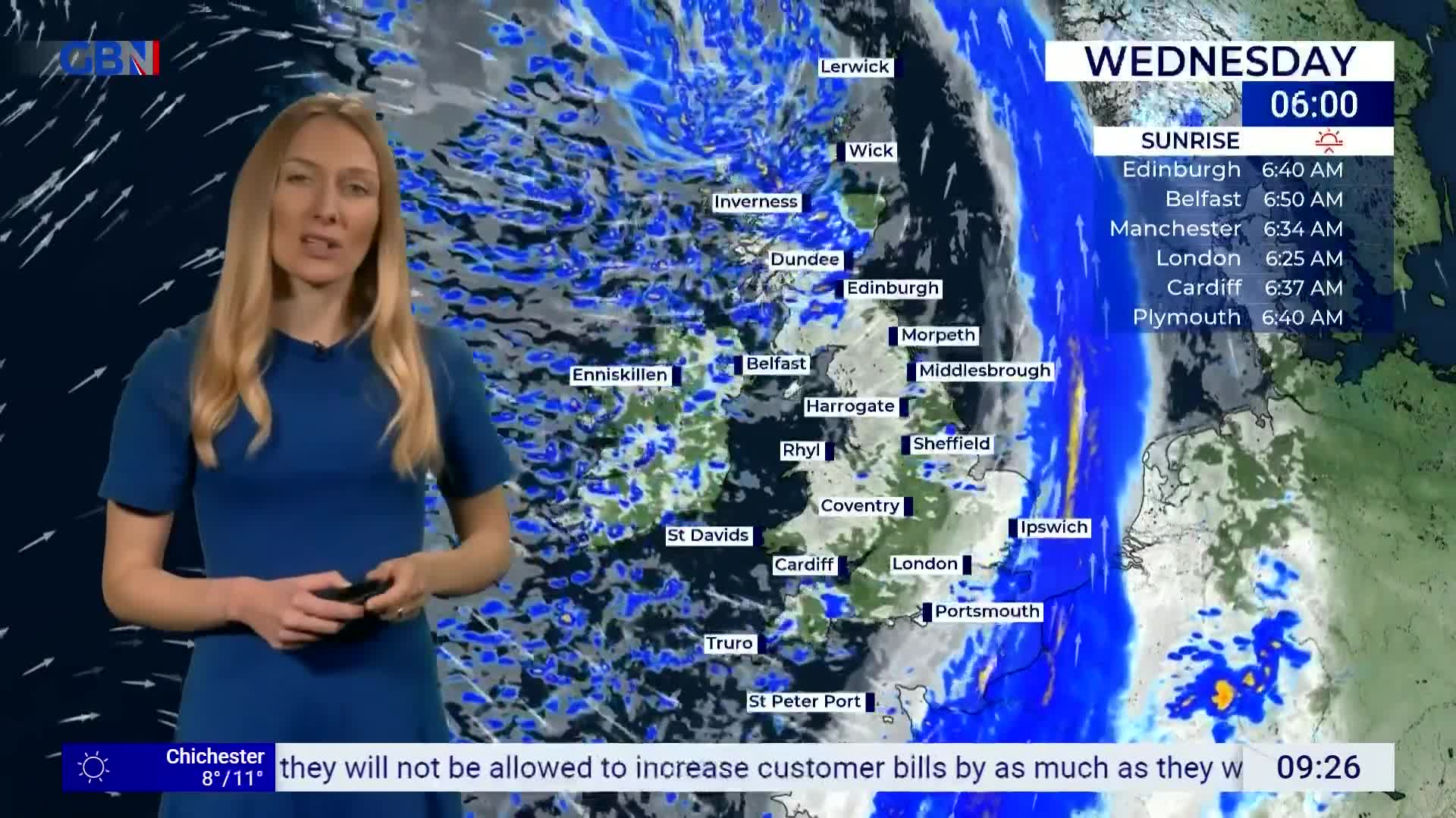 A woman in a blue dress stands before a weather map of the United Kingdom. The map displays a large band of rain moving across the country.