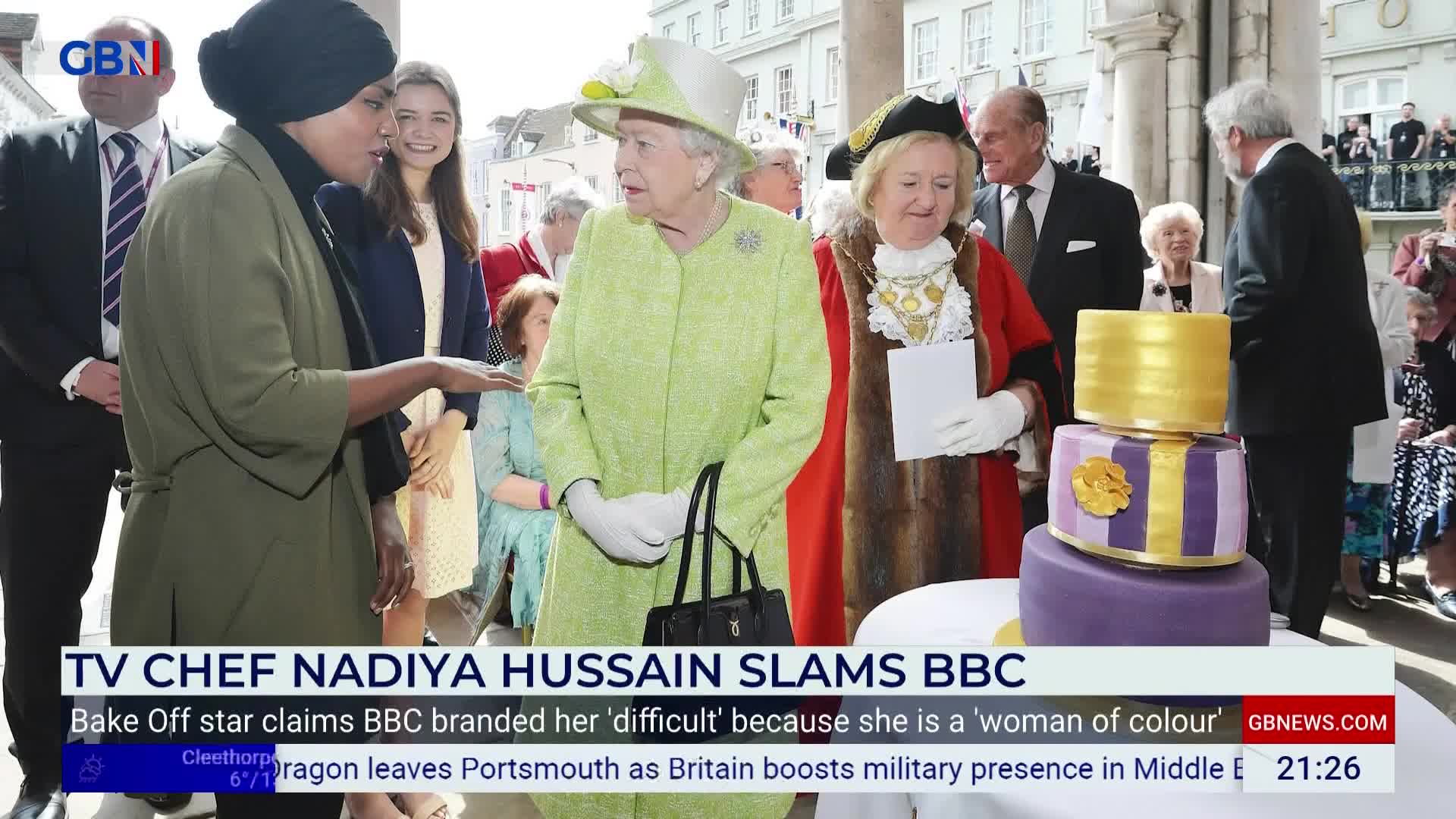 The Queen, in a bright lime green coat, stands beside a woman in ceremonial robes. Nadiya Hussain, wearing a dark headscarf and olive jacket, gestures as she speaks to the Queen.