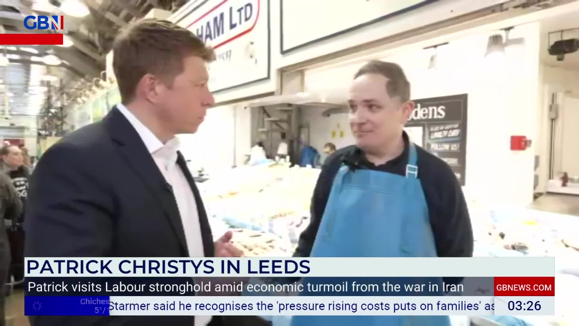 A man in a suit stands facing a man wearing a blue apron, both talking at a market stall. The GB News logo is visible in the top left corner, indicating a broadcast from the United Kingdom. A man in a suit stands facing a man wearing a blue apron, both talking at a market stall. The GB News logo is visible in the top left corner, indicating a broadcast from the United Kingdom.