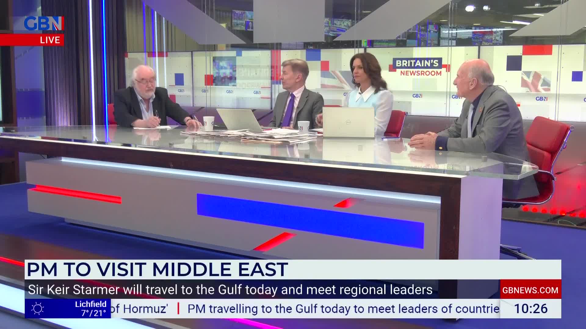 Four people sit at a news desk, bathed in the blue and red glow of the studio lights. A graphic at the bottom of the screen announces "PM TO VISIT MIDDLE EAST." Four people sit at a news desk, bathed in the blue and red glow of the studio lights. A graphic at the bottom of the screen announces "PM TO VISIT MIDDLE EAST."