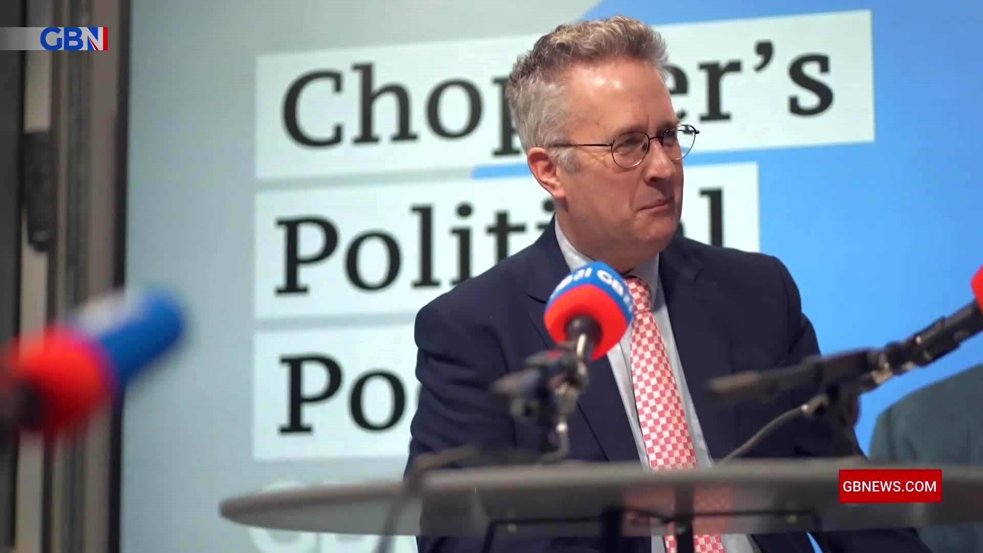 A man in a suit and tie speaks into a microphone at a GB News event. The backdrop behind him displays "Chopper's Political..." A man in a suit and tie speaks into a microphone at a GB News event. The backdrop behind him displays "Chopper's Political..."